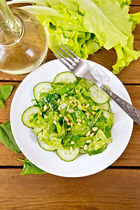 菠菜沙拉新鲜黄瓜鲁科拉沙雪松坚果和春洋葱配有植物油和香料在木板背景上用叉子砸盘图片