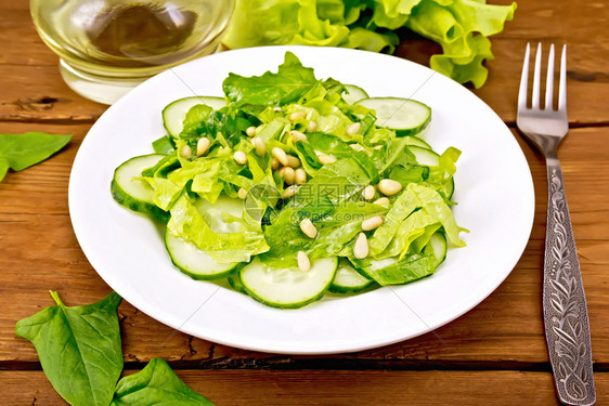 菠菜沙拉新鲜黄瓜鲁科拉沙雪松坚果和春季洋葱盘子里有植物油木板上叉子图片