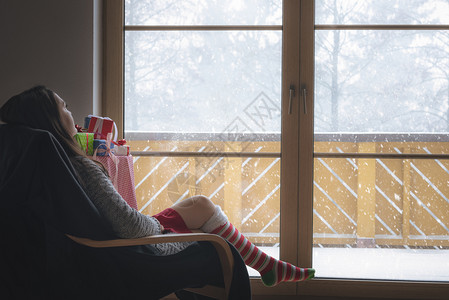 穿着舒适的毛衣长红袜和白子坐在椅上站大玻璃门前看着雪花图片