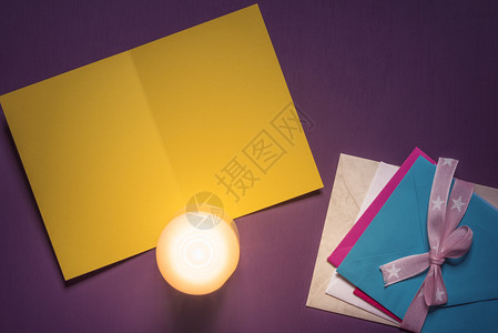 空纸质贺卡上面点燃了蜡烛还有一堆多色信封上面绑着丝带和弓放在紫色木质背景上图片