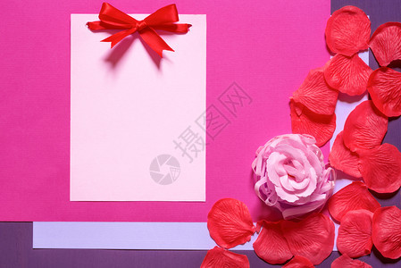 用红弓绑着的无纸留言卡周围是粉红玫瑰和花瓣由肥皂红花瓣和紫色纸背景图片