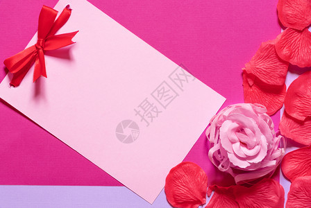 粉红色纸条上面贴着红领结四周环绕着香皂玫瑰和花瓣贴在洋红纸上图片