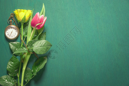 黄玫瑰和粉红色的郁金香洒满了水和古老的口钟在他们身边深绿色背景背景图片