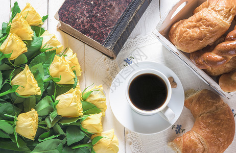 早餐桌一杯咖啡新鲜烤面包旧闭书和一束黄色玫瑰花放在白木桌上图片