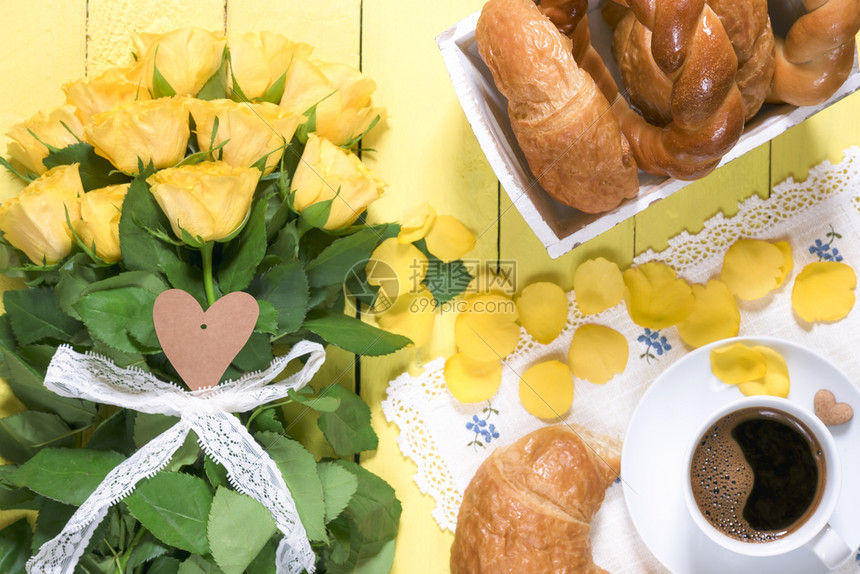 用糕点产品一杯咖啡香味和一束黄色玫瑰花和瓣放在一张黄色木制桌子上图片