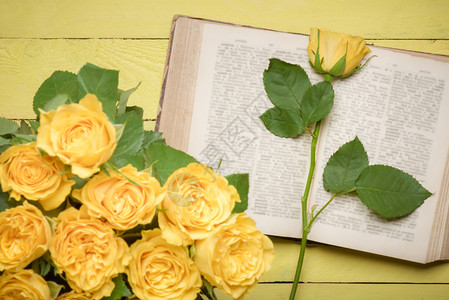 在一本开阔的古典书上美丽单黄色玫瑰展示在黄色的木制桌子上和一束模糊的玫瑰花上在前景中图片