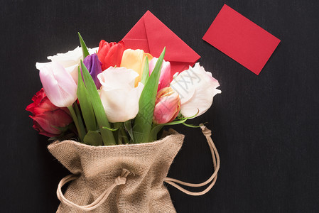 贺卡上挂着一束玫瑰和郁金香的花束包裹在黑木背景的皮上包在一个黑塞袋封闭信和张红色纸上图片