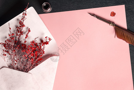 浪漫的框满是红花空白纸页靠近墨水瓶和旧羽毛笔在黑木制桌子上图片