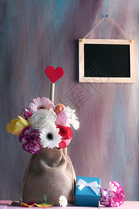 花朵多彩红心的装在黑森包里粉红色桌上的蓝礼物盒紫墙上的黑板图片
