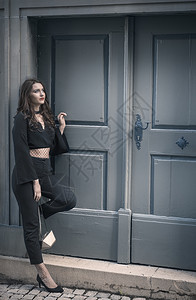 穿着时髦的黑衣服和高跟鞋的年轻美女仰着一扇旧蓝色的木门等待和仰望着图片