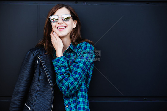黑发女孩身着皮夹克站在城外的黑墙上发女孩身着色岩石皮夹克站在城外的黑墙上图片