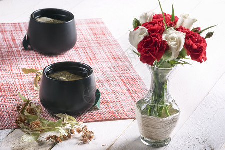 白玫瑰和红康乃馨的花束装在一个可爱的花瓶里和两杯黑茶图片