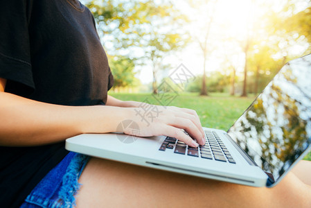 年轻的女用开放式笔记本电脑在绿草上双腿女孩和手放在键盘上远程学习概念在公园里工作笔记本电脑上快乐的时髦年轻女户外学习的生图片