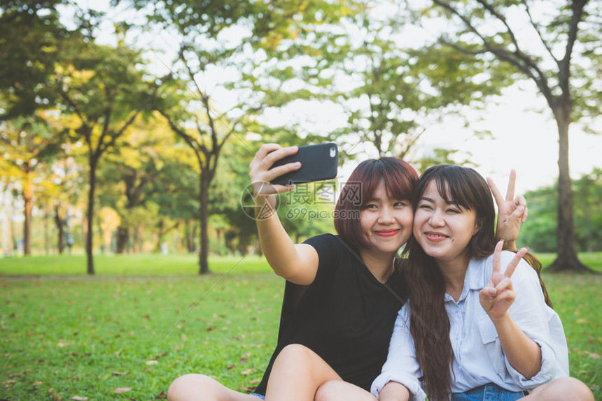 两个快乐的年轻亚洲女朋友一起在公园玩乐和自拍快的年轻亚洲女孩微笑