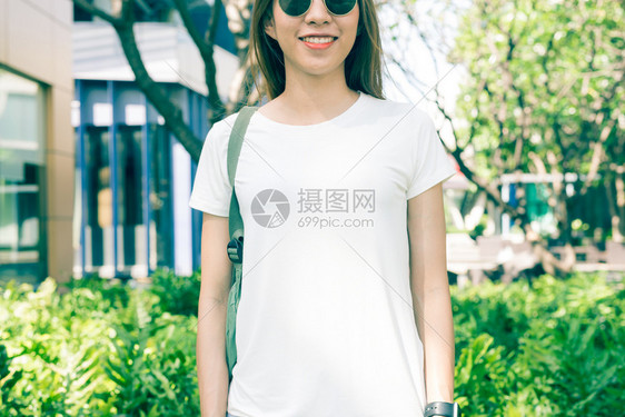 身着白色空t恤的棕长头发亚洲时装女孩站在街上身穿头服装的女站在绿色城市背景上图片