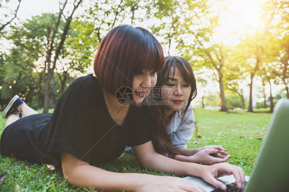 躺在草地上使用笔记本电脑和打字的年轻女孩手握键盘远程学习概念在公园里工作笔记本电脑上工作的快乐年轻女在户外学习的生图片