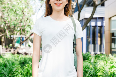 身着白色空t恤的棕长头发亚洲时装女孩站在街上身穿头服装的女站在绿色城市背景上图片