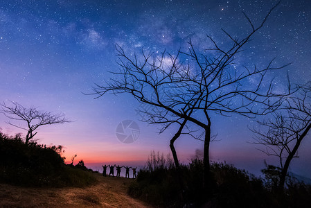 夜晚的天空与星和欢乐的人们一起站立在举手来蓝色的牛奶般天空与山上人在一起与宇宙相背夜晚的风景旅行自由的概念图片