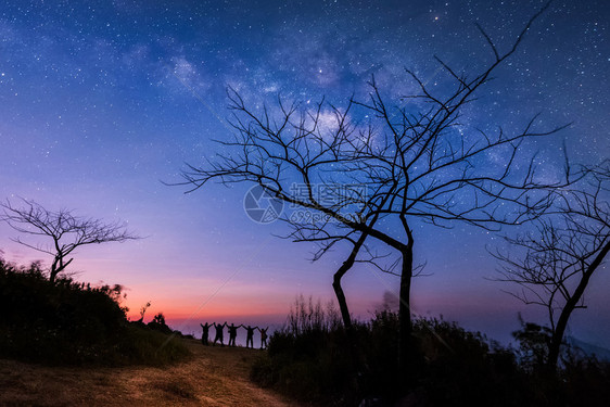 夜晚的天空与星和欢乐的人们一起站立在举手来蓝色的牛奶般天空与山上人在一起与宇宙相背夜晚的风景旅行自由的概念图片