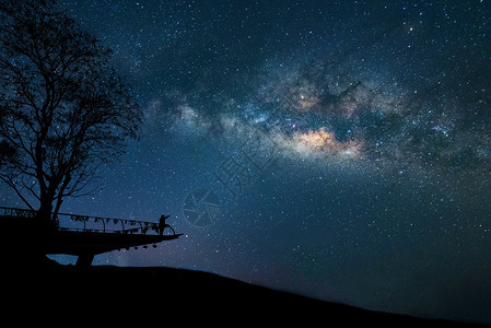 夜空多彩的有星和在山上举起双臂的快乐男士轮廓自由旅行的周末假期长图片