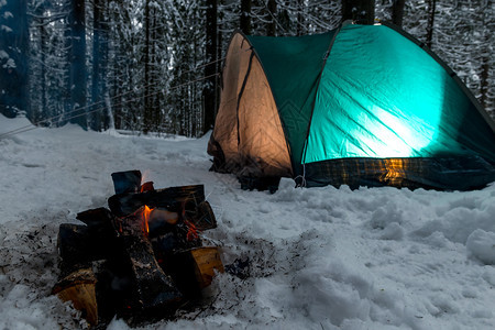 关注冬季森林绿色帐篷背景下雪中火灾的焦点图片