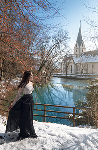 穿着优雅的黑发年轻女人穿着雪衣走过白在blautopf泉边阳光明媚的一天在blauern德国图片
