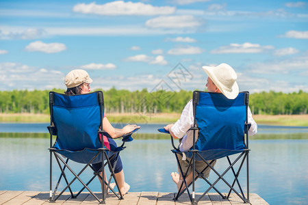从一对夫妇的背面看坐在椅子上木头码的湖附近放松图片