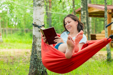 女孩在花园的吊床里读一本书图片