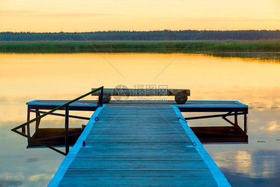 黎明时在光滑的平静湖附近看到一个木制码头图片