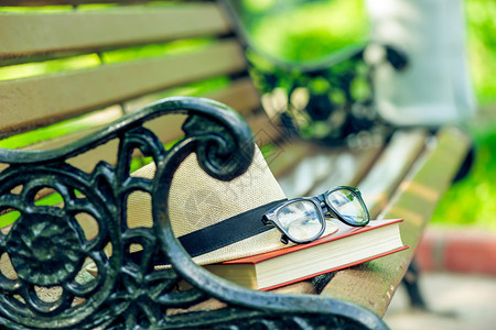 在厚的书上戴眼镜和在公园长椅上被遗忘的草帽图片