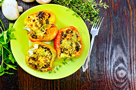 辣椒甜塞满蘑菇西红柿椰菜和奶酪放在餐巾叉子和桌的绿板上辣椒和蘑菇椰菜放在绿色板顶上图片