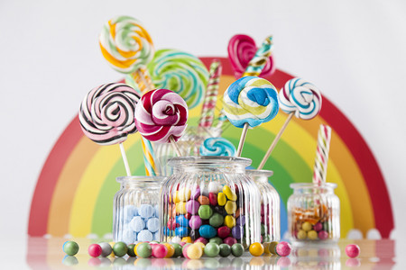 彩虹棒棒糖口香糖球上桌的罐子中彩色糖果棒和口香球中的玻璃罐子背景