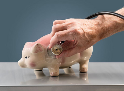 高级男医生或兽检查大粉红猪银行的状况以说明储蓄或退休情况高级男手在猪银行持有听诊器图片
