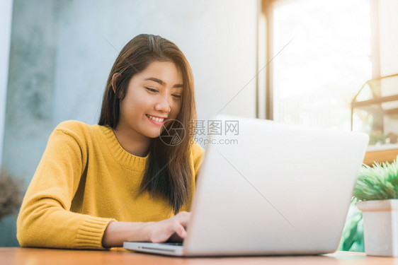 年轻女与她的在桌子上工作年轻女在桌子上工作带着微笑与笔记本一起工作年轻女在周末与笔记本电脑一起工作在温暖的阳光日子里工作笔记本电图片