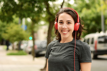 年轻美女的肖像红耳机听音乐户外城市概念图片