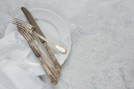 瓷板上的银餐具和白巾纸上带比利时蕾的白餐巾纸在灰色混凝土表面的背有复制空间图片