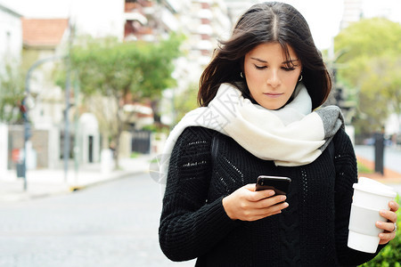 美丽的年轻女子在街上用智能手机发信息图片