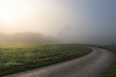 清晨的阳光穿透了迷雾照亮一片绿草原和条乡间公路在斯瓦比什大厅附近德国图片