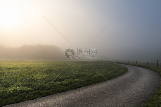 清晨的阳光穿透了迷雾照亮一片绿草原和条乡间公路在斯瓦比什大厅附近德国图片