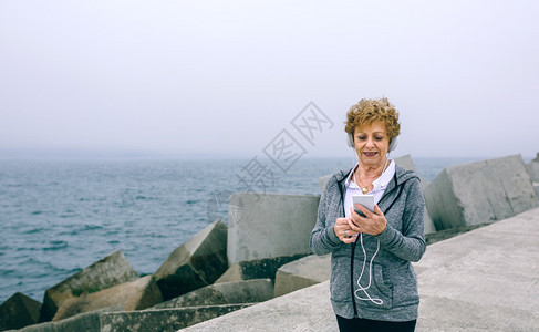 高级运动员用耳机在海上码头看她的智能手机图片