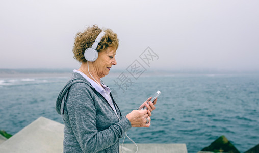 高级女运动员在海上码头使用她的智能手机使用耳的高级女运动员使用她的智能手机图片