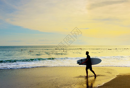 日落时在热带海滩上走着冲浪板的者图片