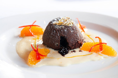 巧克力甜点巧克力味熔岩蛋糕香草酱柑橘白盘上的金叶子图片