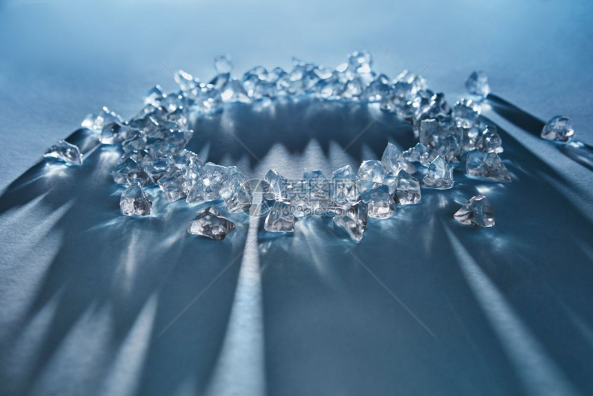 蓝色背景的圆形碎冰块长阴影和反射光从冰的表面反射出来软焦点圆形的
