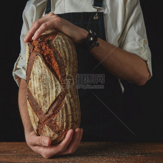 近身的男子和手握着木制桌黑底的全粒新鲜麦面包师和手握着奥瓦尔面包图片