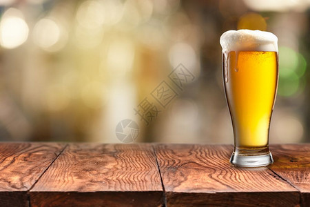 玻璃杯的啤酒在木制桌子上加泡沫背景模糊玻璃杯的啤酒放在木制桌子上背景模糊图片