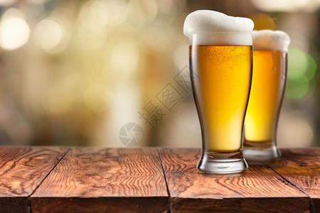 两杯啤酒在空棕色木制桌子上加泡沫背景模糊木制桌子上加两杯啤酒图片