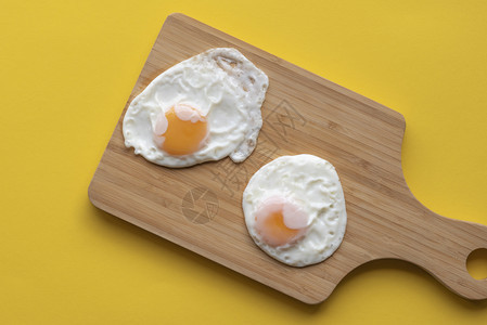 黄色厨房桌上的木切板有两个炸鸡蛋图片