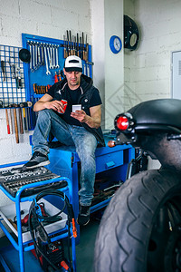 在他的车间里喝啤酒休息的摩托车修理工喝啤酒休息的摩托车修理工图片