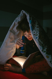 在被子下用手电筒看书的男孩高清图片